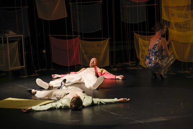 Britta and William in conversation while performing crowd members who have fallen to the floor before the dream sequence dance, with Kasia rehanging banner, Tanzfabrik Berlin, June 2021 – photo by Anja Weber